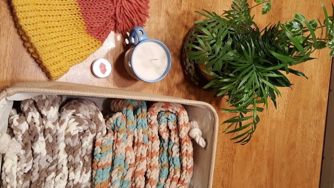 A knit hat. A candle in a cup. A basket with two scarves.